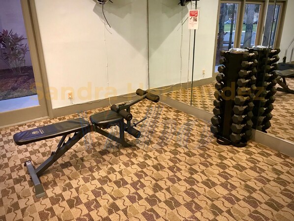 Un gimnasio con una prensa de banca, una jaula para sentadillas y una serie de mancuernas.
