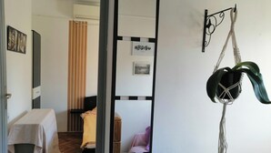 A hotel room with a bed, a small table, a chair, a hanging macrame plant, and a wall-mounted picture frame. - Tiny Romantic Flat in the Centre (Belgrade)