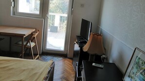 A room with a bed, a desk, a chair, a TV, and a balcony door. - Tiny Romantic Flat in the Centre (Belgrade)