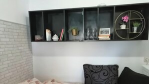 A bedroom with a bed, a pillow, a bedside table, a shelf with books and decorative items, and a brick wall. - Tiny Romantic Flat in the Centre (Belgrade)