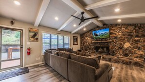 Una sala de estar con chimenea de piedra, un sofá seccional grande y un televisor montado en la pared.