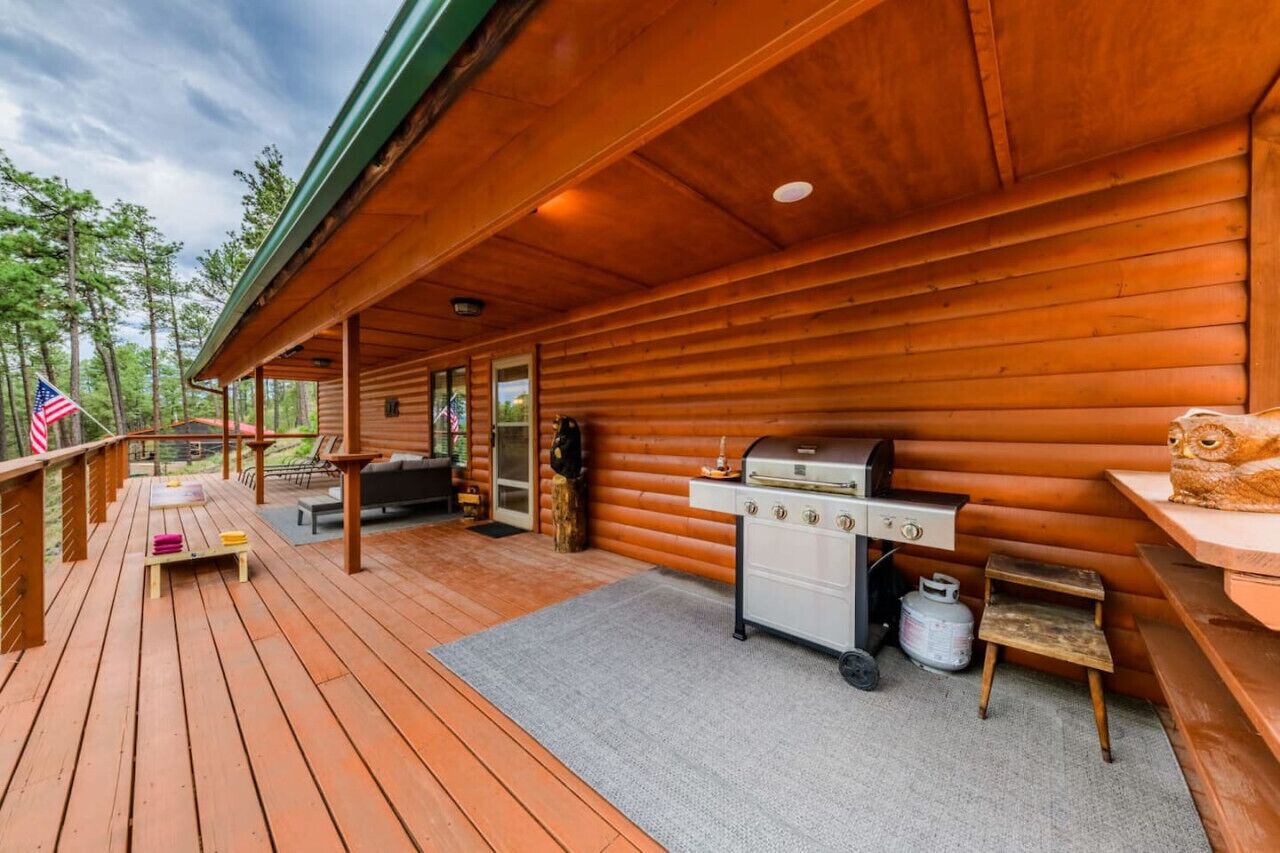 En træhytte med overdækket terrasse, grill og et amerikansk flag.