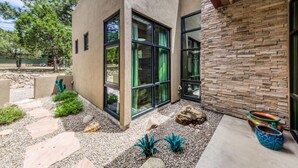 A modern building with large glass windows, a stone facade, and a landscaped garden with rocks and plants. - This Is It -Gorgeous Southwest Modern Luxury! (Alto)