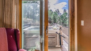 A sliding glass door leading to a hot tub area with a stone surround and a metal railing. - Wine & Wilderness: MTN Luxe Chalet/ Hot Tub/ Views (Ruidoso)