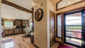 A spacious kitchen with wooden cabinets, a dining area, and a large sliding glass door leading to a balcony with a view of the outdoors. - Wine & Wilderness: MTN Luxe Chalet/ Hot Tub/ Views (Ruidoso)