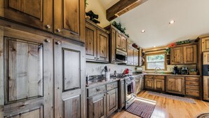 A spacious kitchen with wooden cabinets, a central island, and a large window providing natural light. - Wine & Wilderness: MTN Luxe Chalet/ Hot Tub/ Views (Ruidoso)