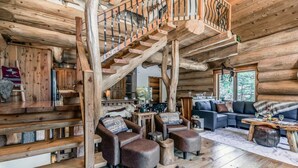 A log cabin interior with a wooden staircase, leather furniture, and a cozy living area. - Bearfoot Lodge: Hot Tub, Pets, River & Trails (Ruidoso)