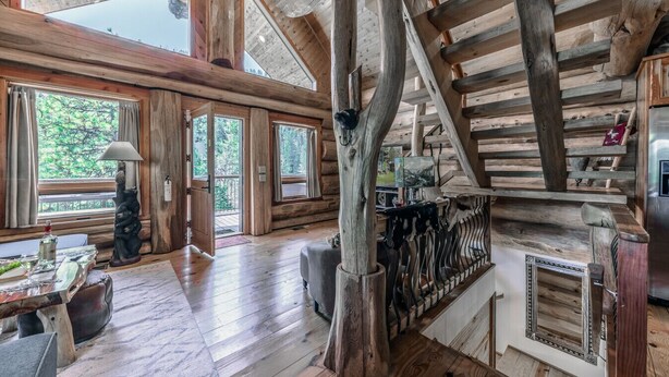 A spacious log cabin interior with large windows, a fireplace, and a dining area. - Bearfoot Lodge: Hot Tub, Pets, River & Trails (Ruidoso)
