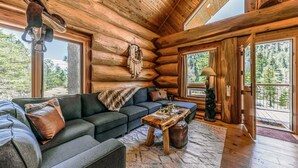A log cabin interior with a sofa set, a wooden coffee table, and a bear statue. - Bearfoot Lodge: Hot Tub, Pets, River & Trails (Ruidoso)