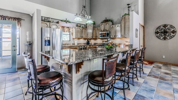 Een ruime keuken met een groot eiland, barkrukken en een decoratief wandobject.