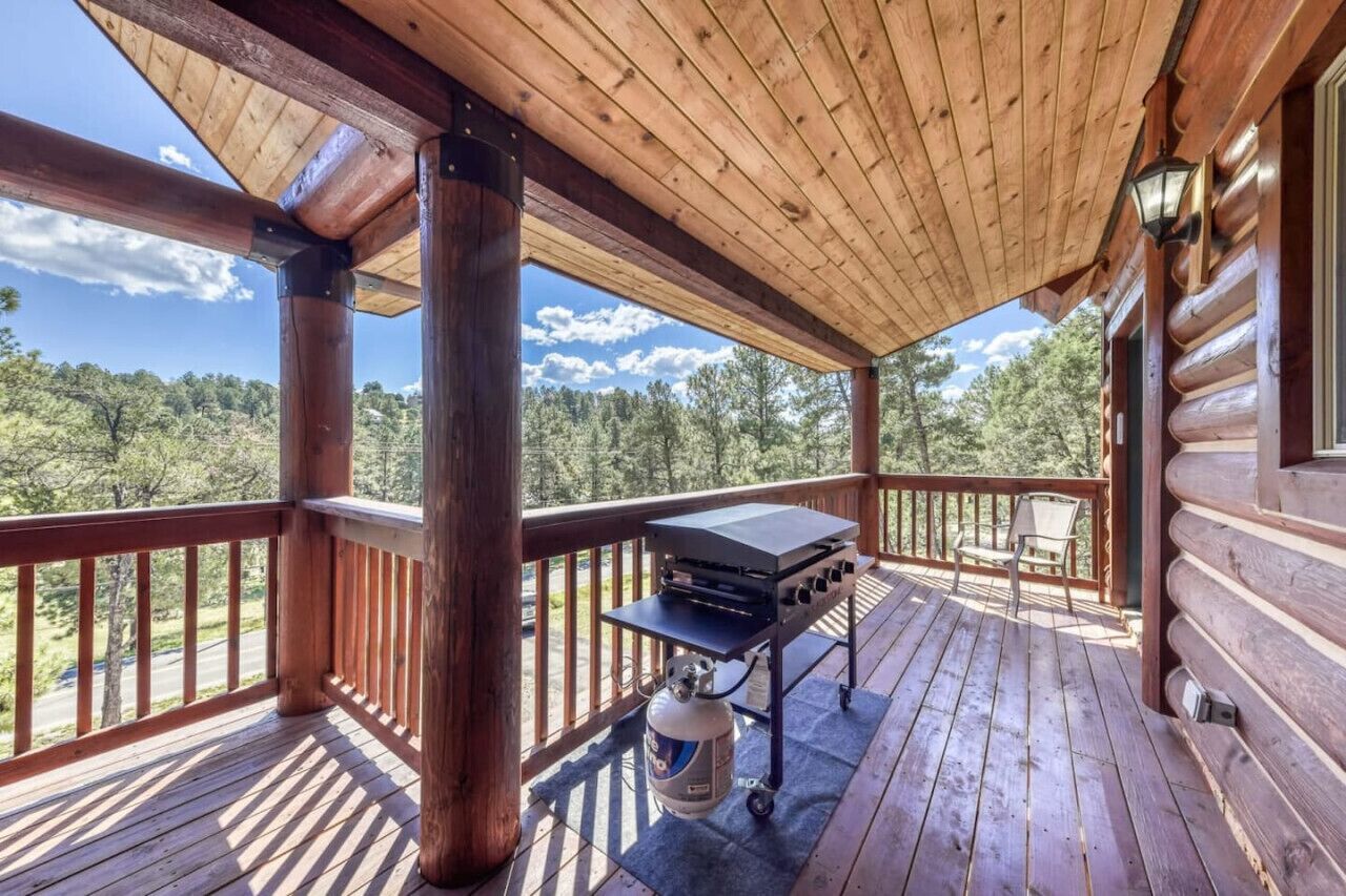 A wooden deck with a grill and propane tank, overlooking a forested area.