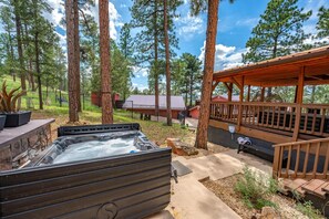 A hot tub in a wooded area with a wooden deck and a covered seating area.