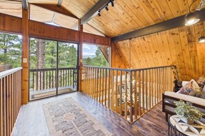 Un interior de madera con un balcón, una escalera y una zona de estar con cojines.