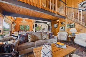 Interior acogedor de una cabaña con una escalera de madera, un conjunto de sofás y una mesa de comedor.