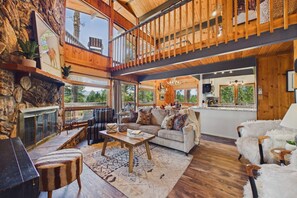 Amplia sala de estar con chimenea, un conjunto de sofás y un comedor con cocina al fondo.