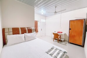 A hotel room with a bed, a desk, a chair, a wardrobe, and a ceiling fan. - Orien Guest House By Helocus (Pematangsiantar)