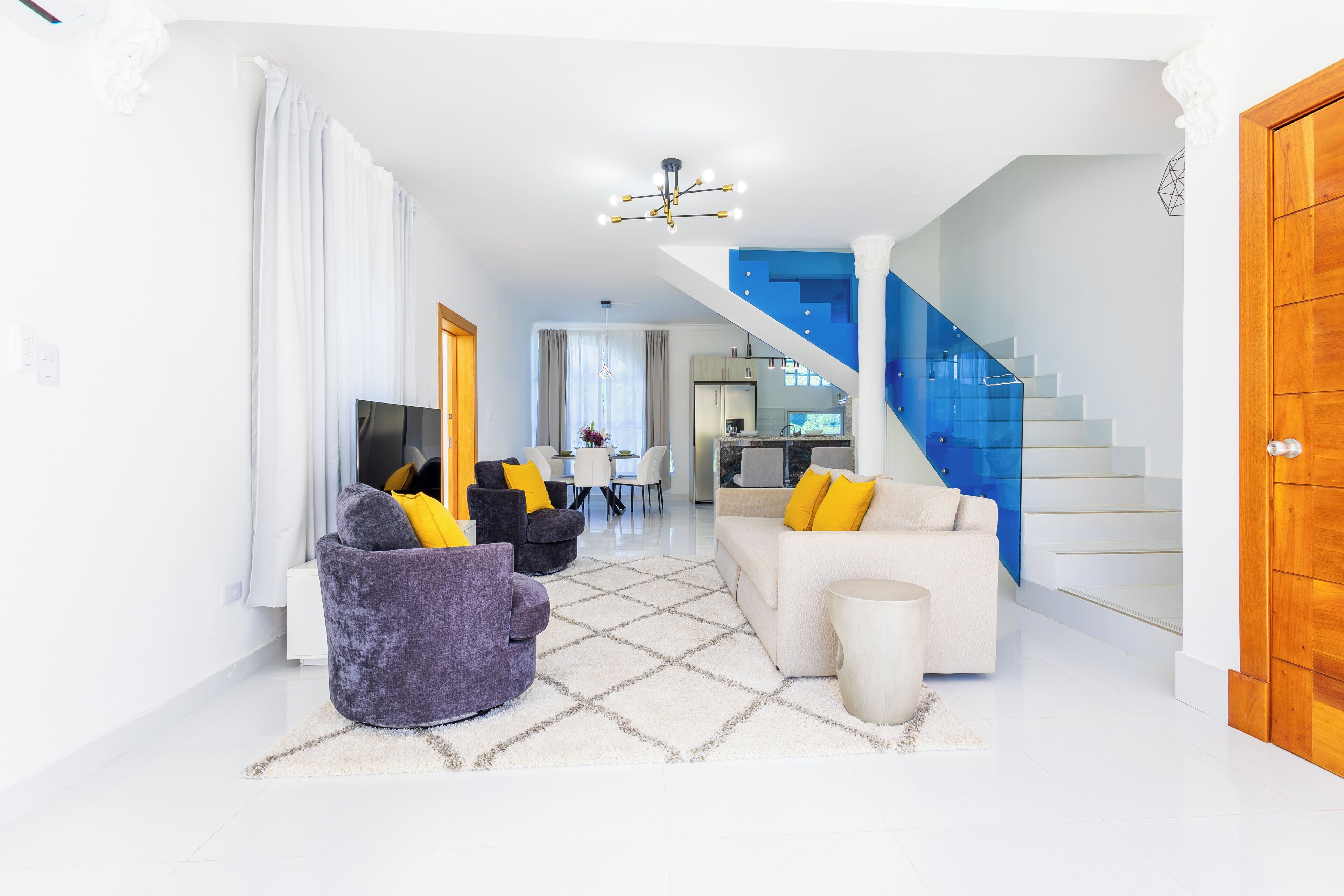 A modern living room with a sofa, armchair, and a coffee table. There is a staircase with blue steps leading to an upper level.
