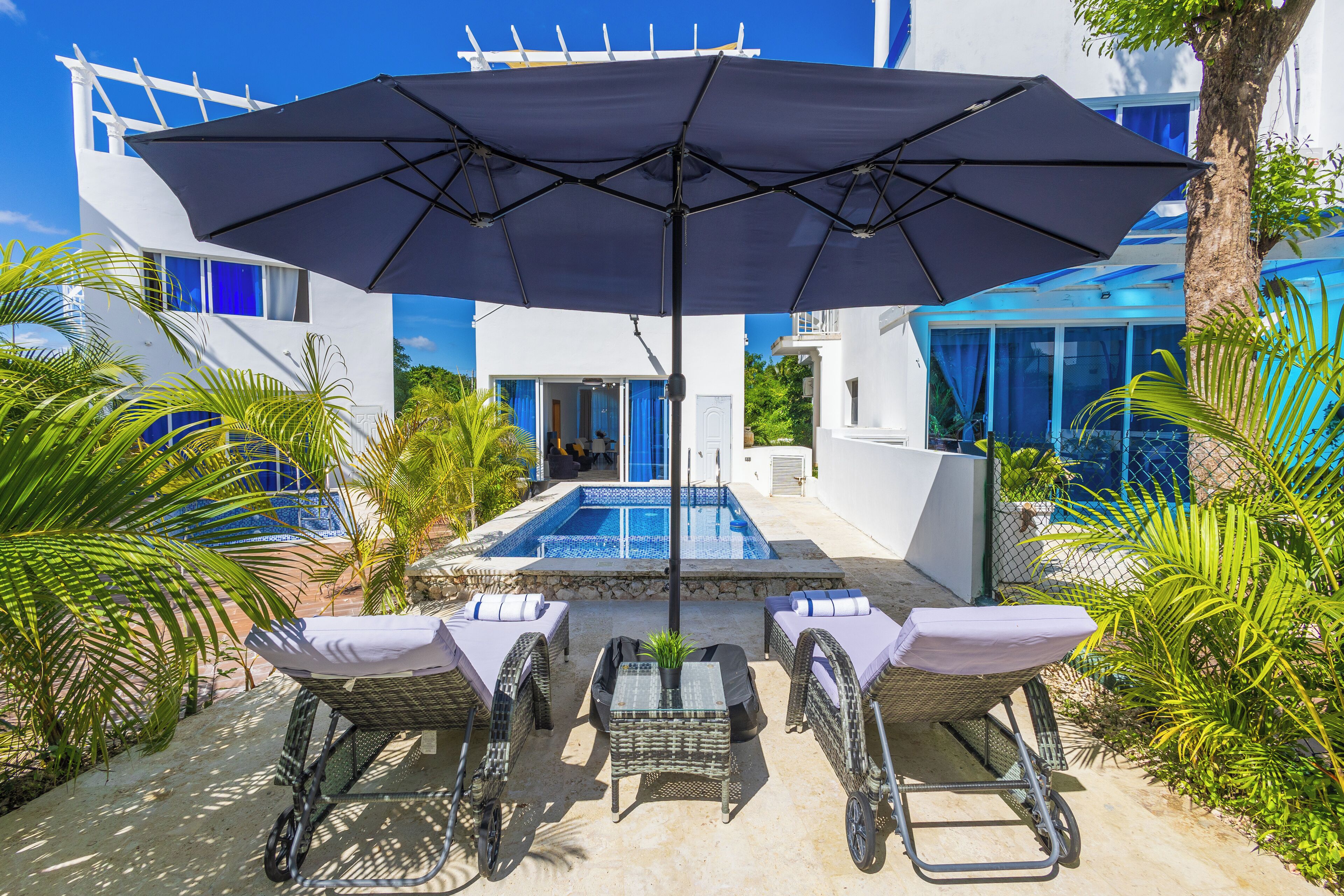 Uma área à beira da piscina com espreguiçadeiras, uma mesa e um guarda-sol.