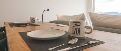 A dining table set with plates, cutlery, and a mug, with a view of mountains through a window.