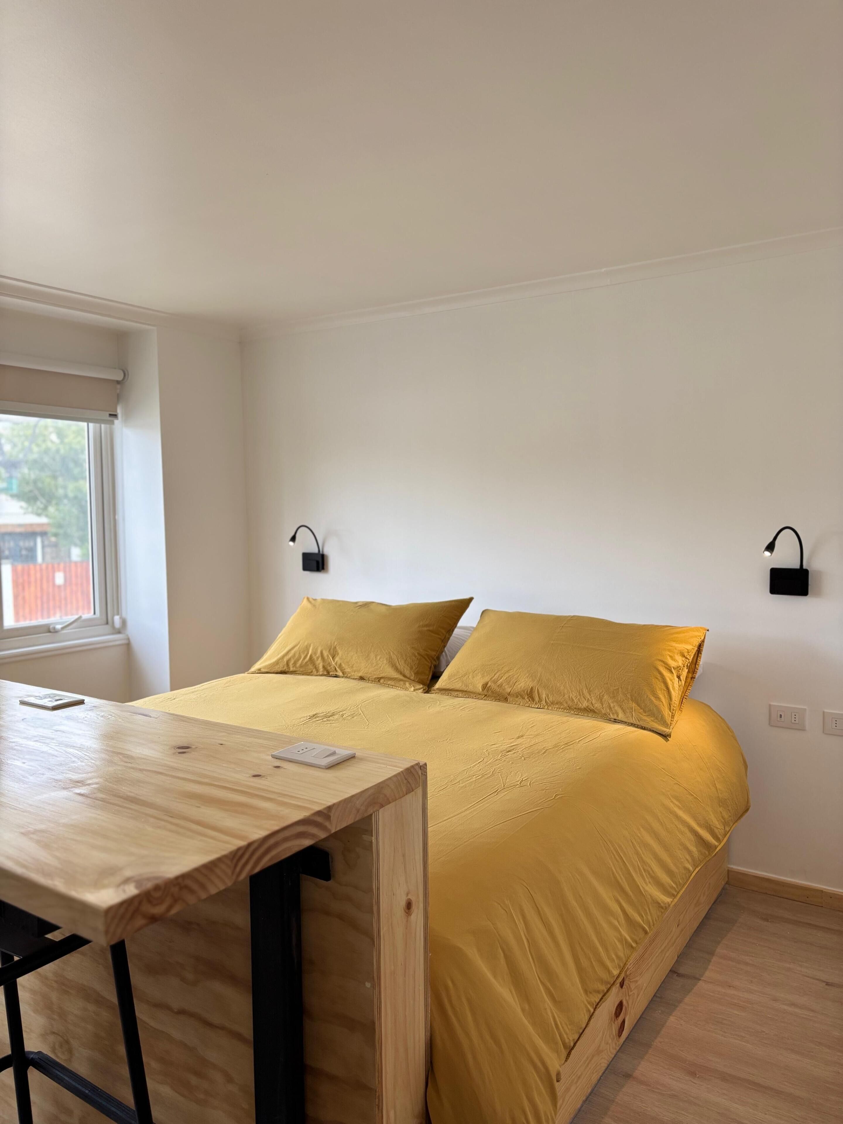 Un dormitorio con una cama, un escritorio de madera y dos lámparas de pared.