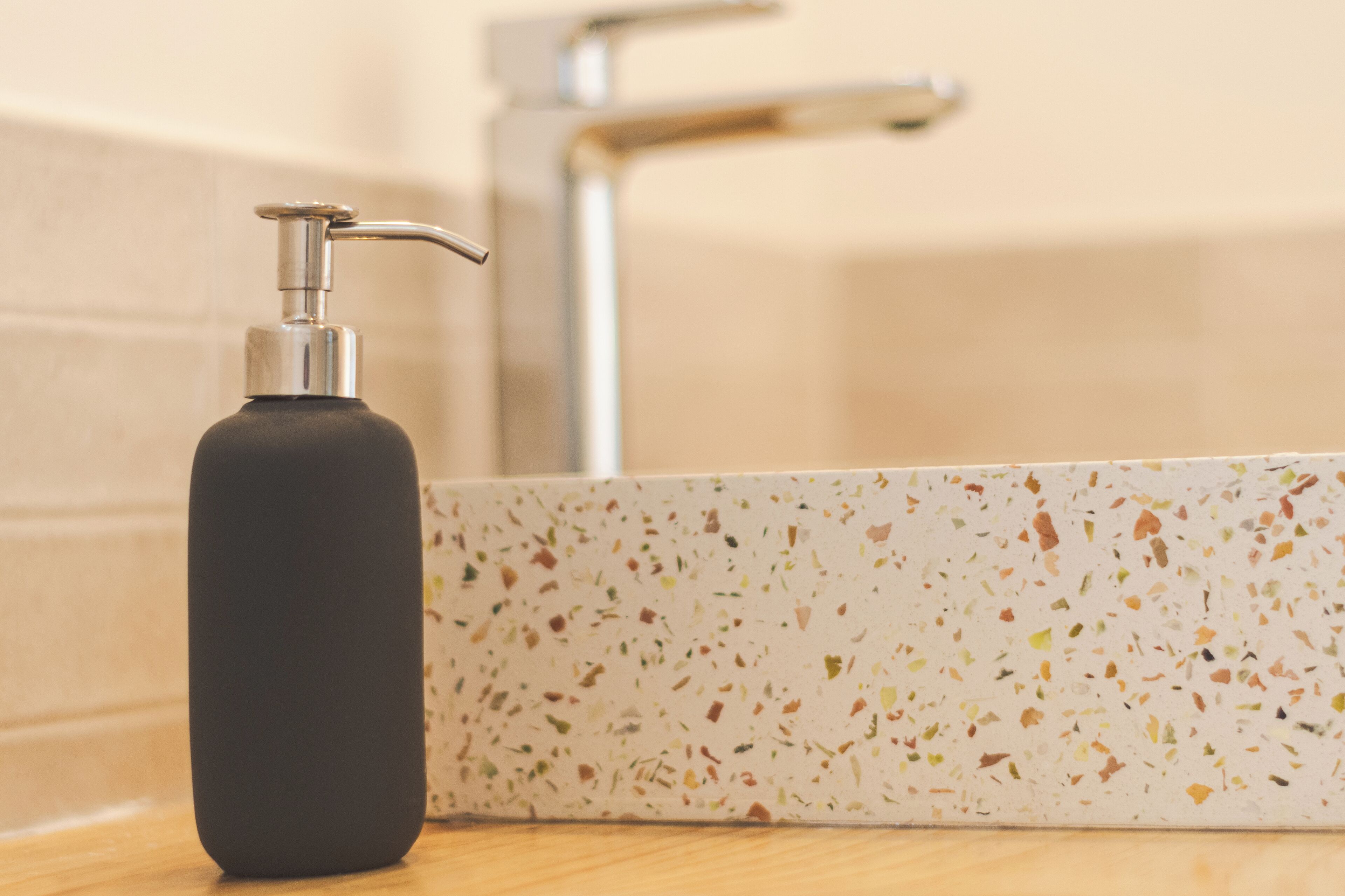 A bathroom with a black soap dispenser and a speckled tile sink.