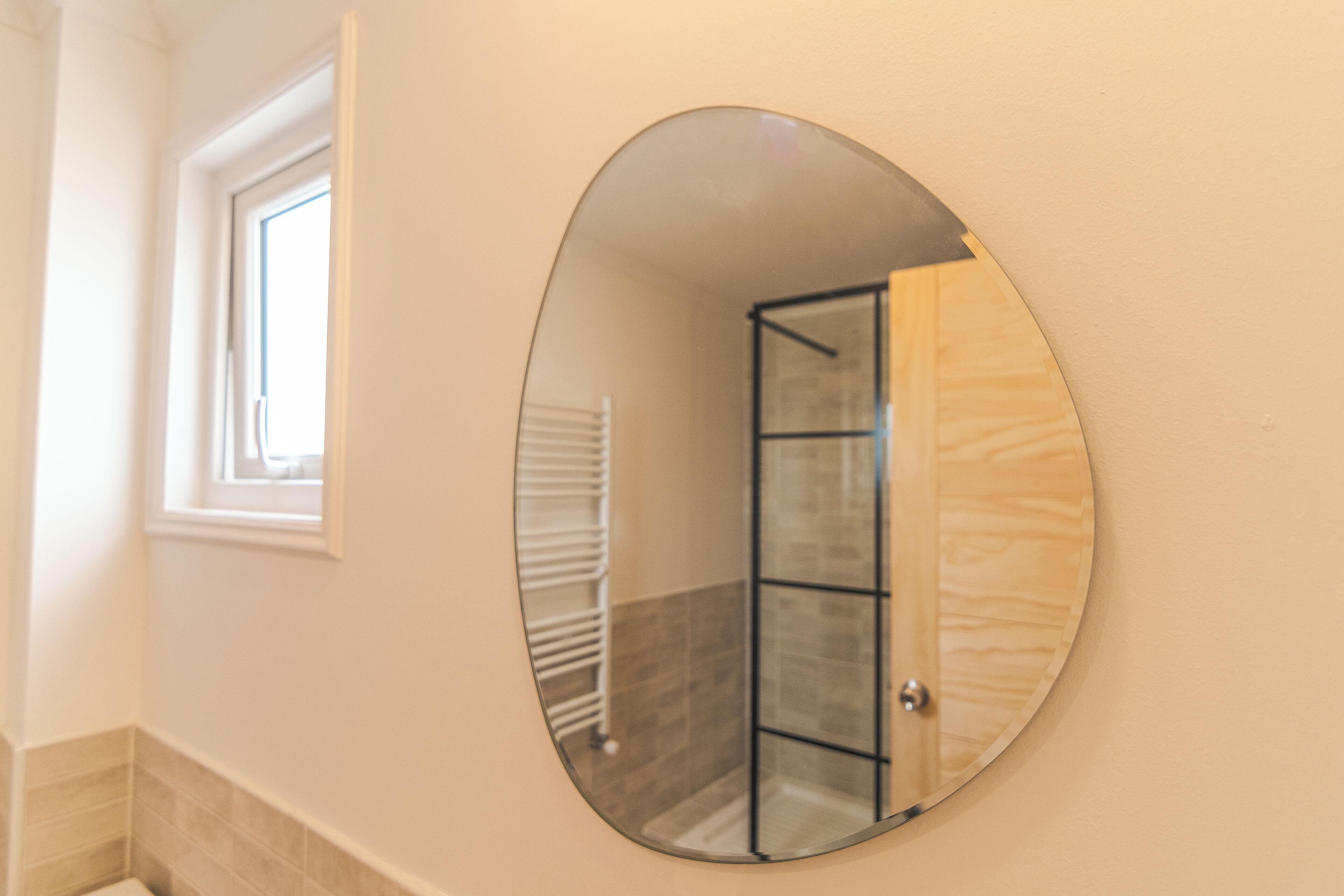 A bathroom with a round mirror, a shower, and a window.