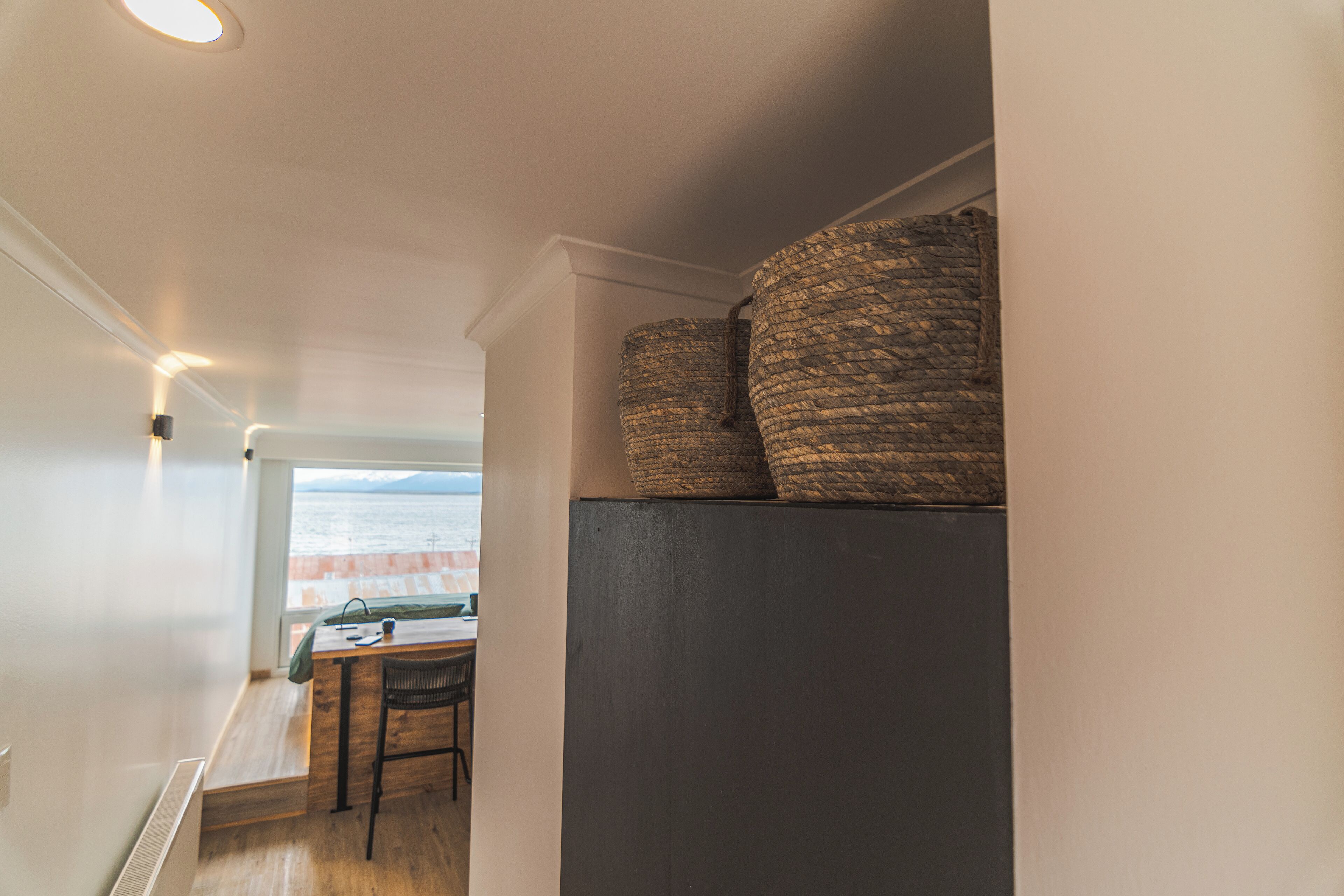 Una habitación con vistas al mar, un escritorio de madera y dos cestas tejidas sobre un mueble oscuro.