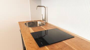A kitchen with a stainless steel sink, a black induction cooktop, and wooden countertops.