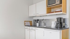 Een moderne keuken met witte kastjes, een magnetron, een koffiezetapparaat en een snijplank.