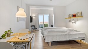 Een moderne slaapkamer met een bed, een bureau met stoel, een potplant en een raam met uitzicht.