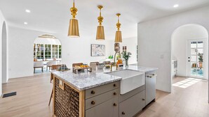 A spacious kitchen with a marble countertop, three pendant lights, and a large island.