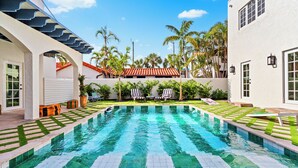 A swimming pool with a geometric tile pattern, surrounded by lounge chairs and palm trees.