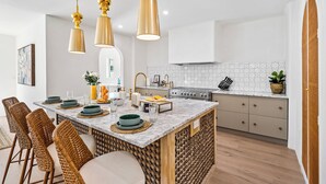 A modern kitchen with a marble island, gold pendant lights, and a white backsplash.