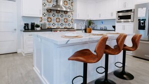 Una cocina moderna con armarios blancos, un salpicadero estampado, electrodomésticos de acero inoxidable y una isla central con taburetes de bar.