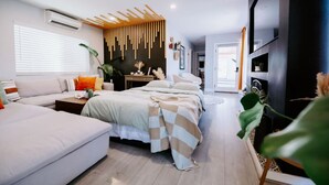 Un dormitorio moderno con sofá, dos camas, televisor y un ventanal grande.