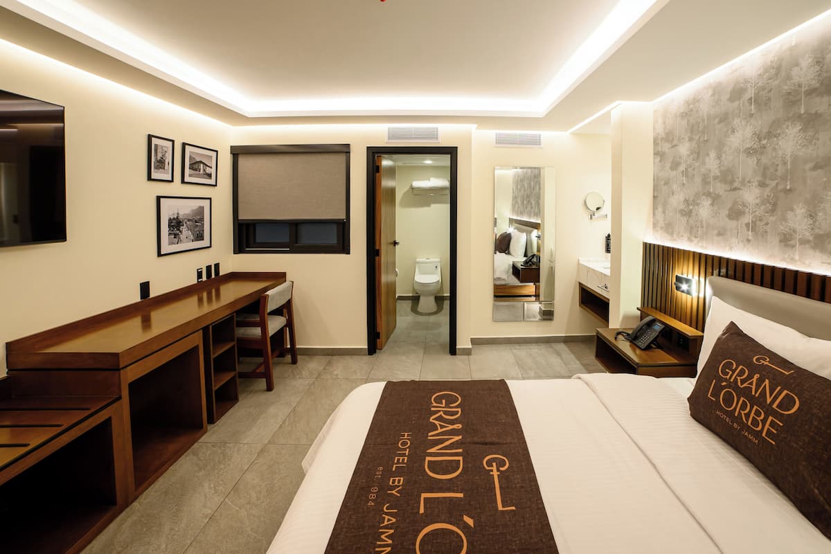 A hotel room with a bed, a desk, a chair, a bathroom, and a mirror.