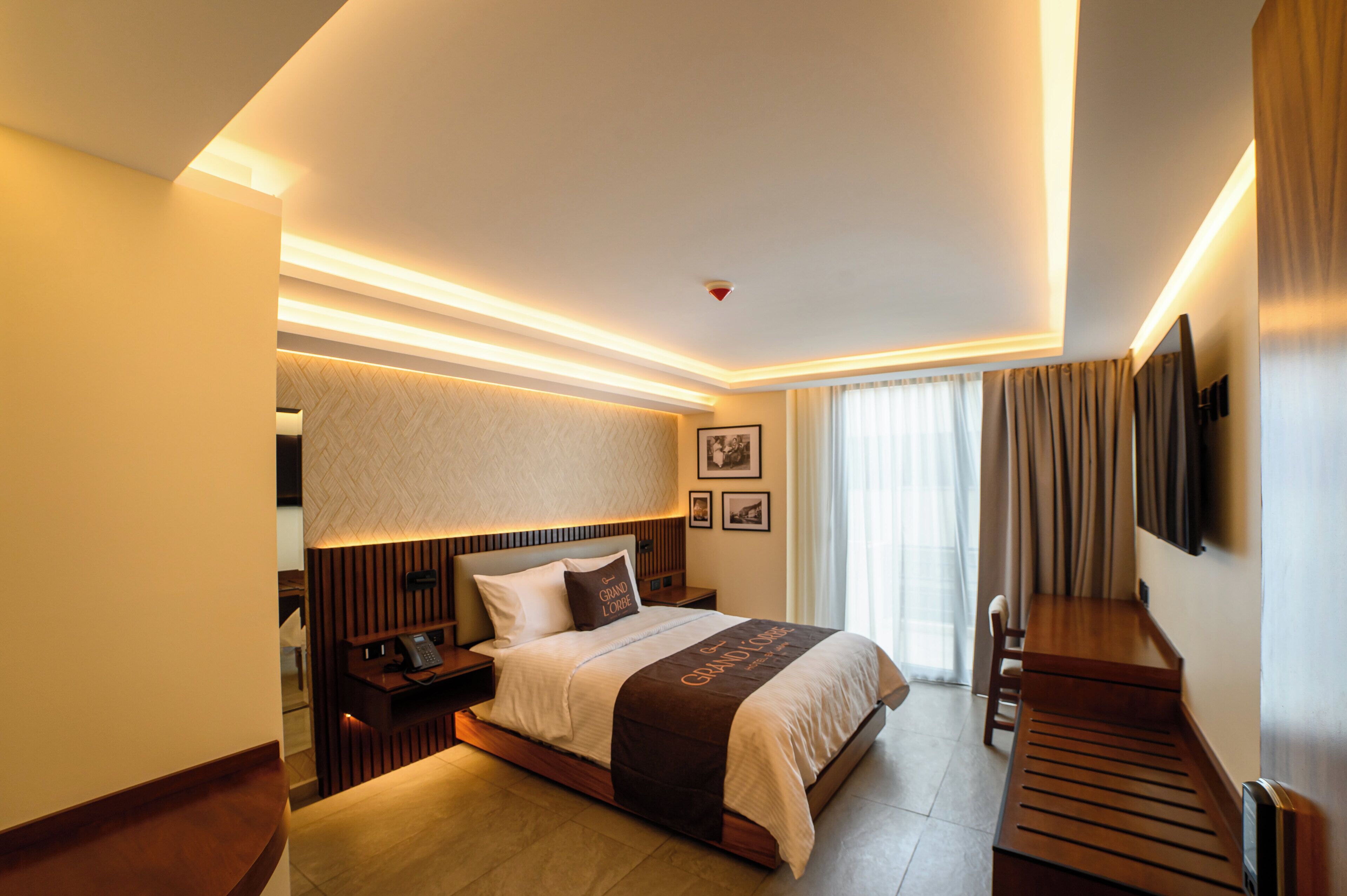 A modern hotel room with a large bed, bedside tables, a desk, and a television.