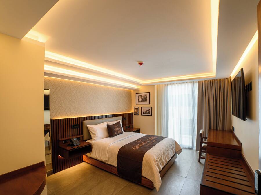 A modern hotel room with a large bed, bedside tables, a desk, and a television.