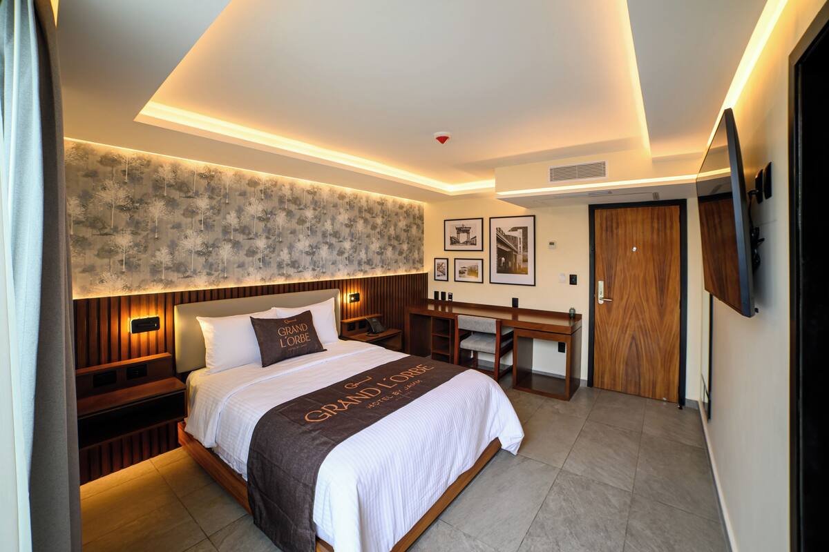 A hotel room with a large bed, a desk, and a mirror.