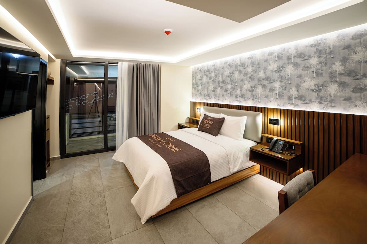 A modern hotel room with a large bed, a desk, and a TV.