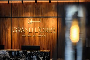A reception desk with a wooden panel wall displaying the name "GRAND L'ORBE HOTEL BY JAMM". - HOTEL GRAND LORBE by JAMM (Orizaba)