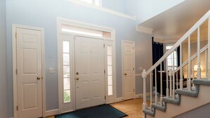 A hallway with three white doors, a blue doormat, and a staircase with white railings.