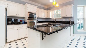 A kitchen with white cabinets, a black countertop, a gas stove, a microwave, and a window with a view.