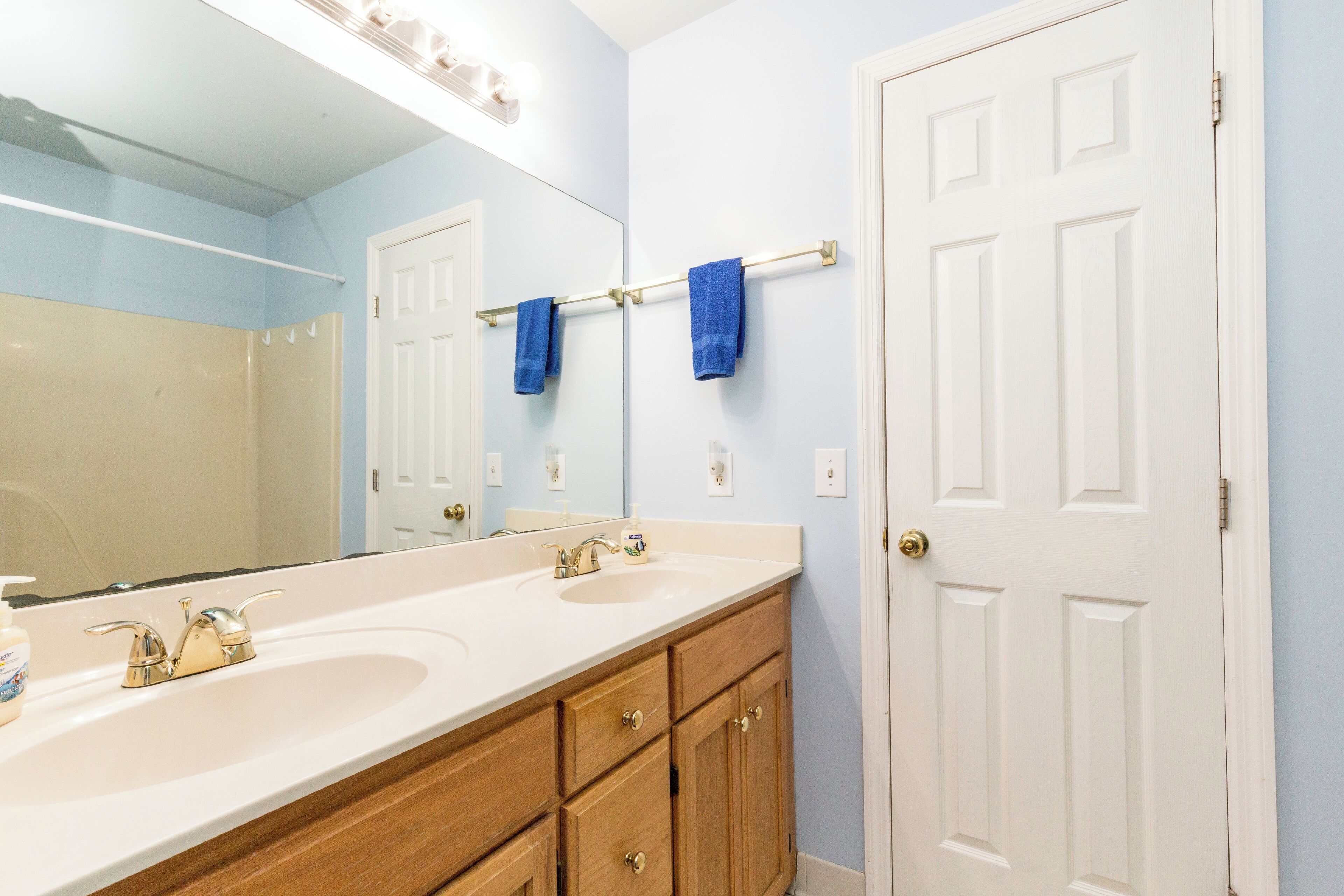 Une salle de bain avec deux lavabos, des meubles en bois, un porte-serviettes et une porte blanche.