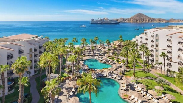 Un complexe hôtelier doté d’une piscine, de palmiers et offrant une vue sur l’océan et un navire.