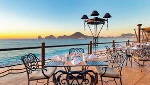 Un espace de restauration en plein air, avec des tables et des chaises, offrant une vue sur la mer et le coucher du soleil.