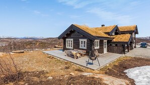 Una baita in legno con tetto di paglia, un patio in legno e vista sulle montagne sullo sfondo.