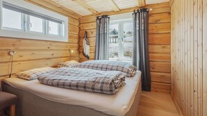 Una camera da letto accogliente in una baita di legno, con un letto, una lampada da comodino e una finestra con tende.