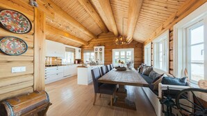 Un ampio interno di una baita in legno con un grande tavolo da pranzo, pavimenti in legno e un'accogliente zona salotto vicino alla finestra.