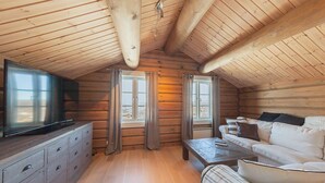 L'interno accogliente di una baita di legno, con travi a vista, un televisore su un comò, un divano e due finestre con tende.